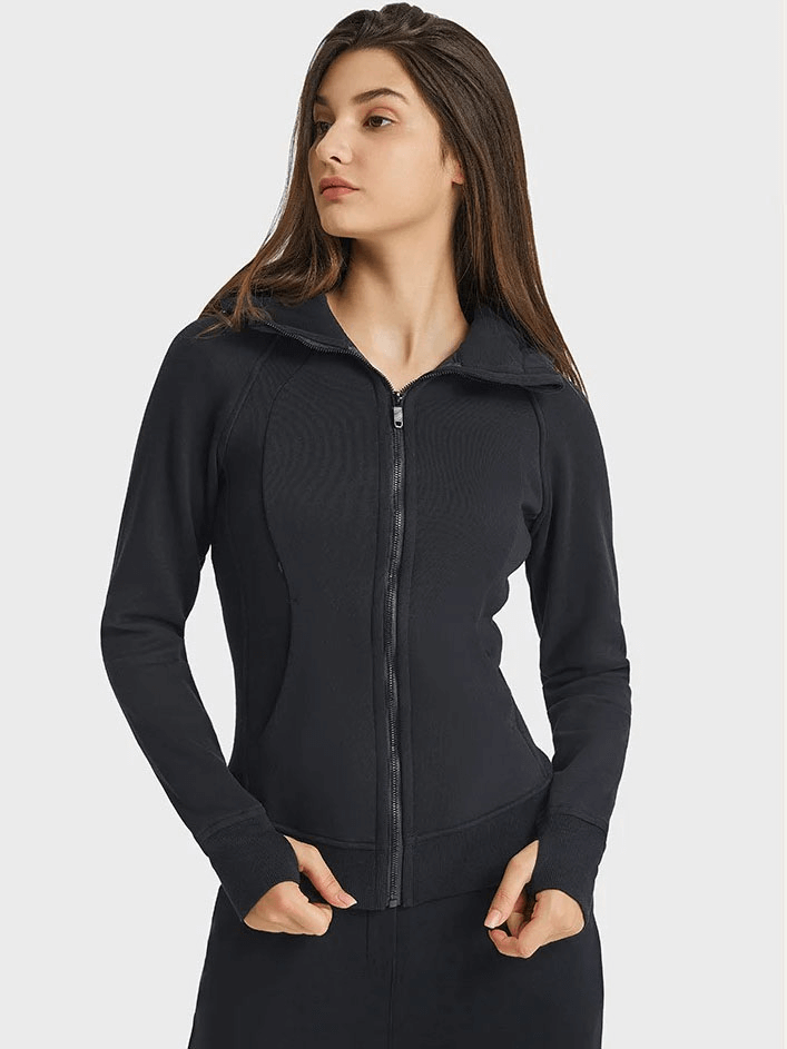 Woman wearing a black zip-up athletic fleece hoodie with a stand collar, hands in pockets, showcasing comfortable and stylish activewear.